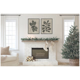 White brick fireplace with pine garland and two stockings hanging, flanked by two windows and a decorated pine tree in a woven basket on the right.