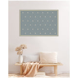 Framed blue botanical block print with white floral motifs, hung above a light wooden bench with neutral pillows and a beige throw in a minimal room.