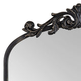 Top corner of a curved arch mirror with an ornate black frame featuring detailed scroll and leaf motifs