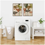 Two framed botanical prints with abstract leaves in earthy tones of brown, green, and rust, hung above a white front-loading washing machine in a minimalist laundry room.