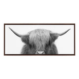 Black and white frontal close-up of a Highland cow with long hair covering its eyes and wide horns, set in a dark wooden frame against a white background.