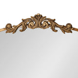 Arched mirror top edge with gold-toned ornate carved scroll and leaf design on a light wood frame