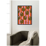 Framed wall art with brown olive shapes and pink star details on vertical coral and pink stripes, hung above an olive green armchair with a cream knit throw.