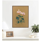 Framed canvas art print of Odilon Redon's 1916 Cyclamen showing pink cyclamen flowers with green spotted leaves on a brown background, hung on white wall over a white table.