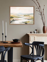 Tranquil landscape painting with soft beige, cream, and green tones framed in a beaded wooden frame, hanging above a beige fireplace in a minimalist room.