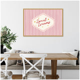 Framed canvas with retro-style ‘Sweet Dreams’ text in pink and red script on vertical pink and white stripes, hanging above wooden dining table and white chairs.