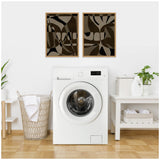 Two framed abstract canvases with organic black, brown, and beige shapes hang side-by-side on a white wall above a white washing machine in a laundry room.