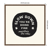 Black circular shape with white text reading 'Slow Down You're Doing Fine maintain the vibes,' framed in simple dark wood on a cream background.