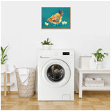 Framed canvas print of a colorful hen with chicks on teal background hanging above a white front-loading washing machine in a laundry room with plants and woven basket.