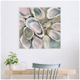 Square canvas painting of overlapping oyster shells in soft pastel shades of pink, blue, and green, framed and hung above a light wooden desk with a plant and decor.