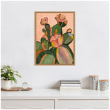 Framed canvas painting of green cactus plants with pink blossoms on a muted peach background, hung above a white shelf with books, plants, and patterned containers.