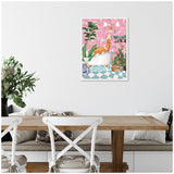 Colorful framed canvas of a brown llama lounging in a white bathtub surrounded by lush green plants with a pink floral wallpaper background, hung above a rustic wooden dining table.