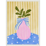 Pink vase with vertical white stripes and blue-and-white striped bow, holding green leaves, set against vertical beige stripes and a blue polka-dot tablecloth.
