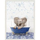 Young elephant playfully sitting in a blue clawfoot bathtub filled with bubbles, against a white wall with blue leafy patterned wallpaper and blue patterned tile floor.