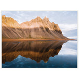 Jagged mountain peaks bathed in golden sunset light, reflecting clearly in still water with a partly cloudy sky above, creating a symmetrical natural scene.
