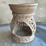 Carved soapstone essential oil burner with open arch design and leaf patterns, featuring a shallow bowl on top and speckled beige stone texture.