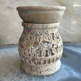 Carved soapstone essential oil burner with intricate leafy patterns and cutouts, featuring a shallow bowl on top for holding oils, carved from beige and brown stone.
