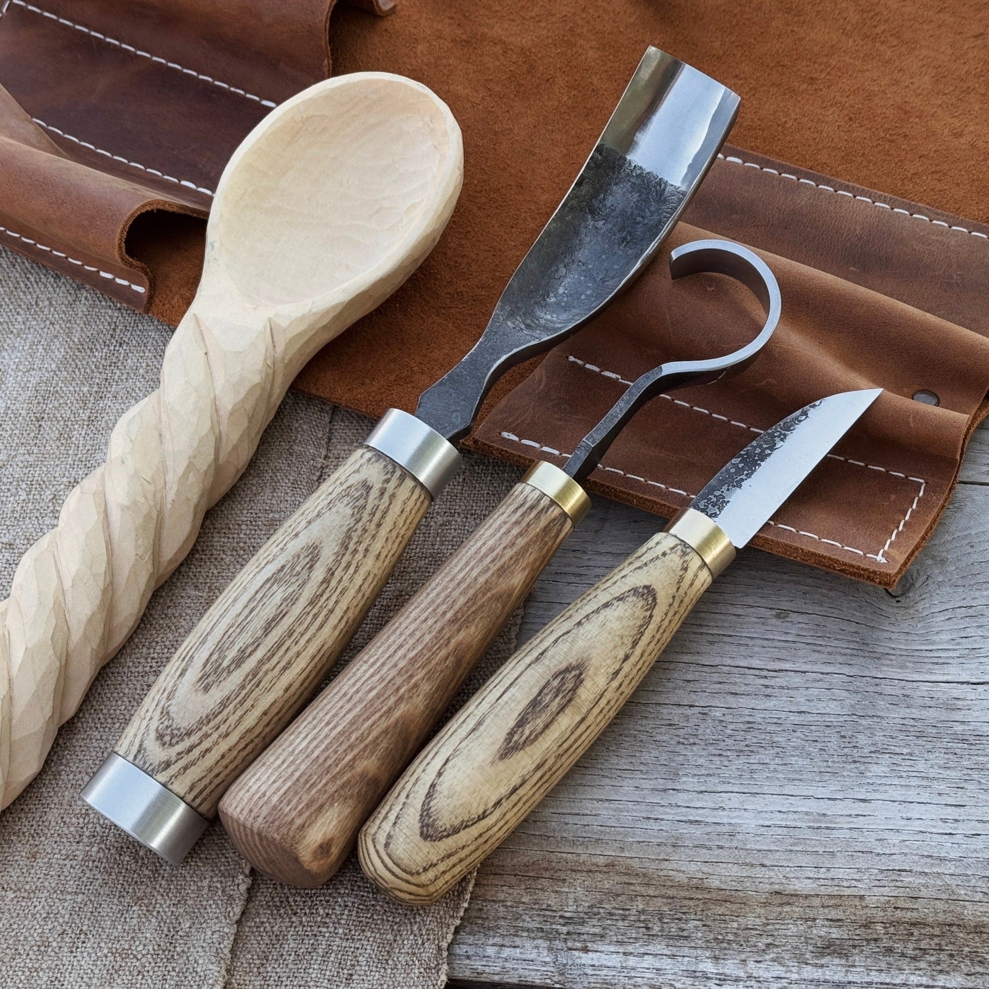 3-piece spoon carving set with leather roll by Sharky Forged Steel Tools showing hook knife, whittling knife, bent gouge, and leather storage roll