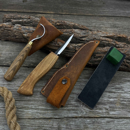 3-Piece Spoon Carving Tool Set with Leather Strop by Sharky Forged Steel Tools showing hook knife, sloyd knife, and leather strop on wooden surface