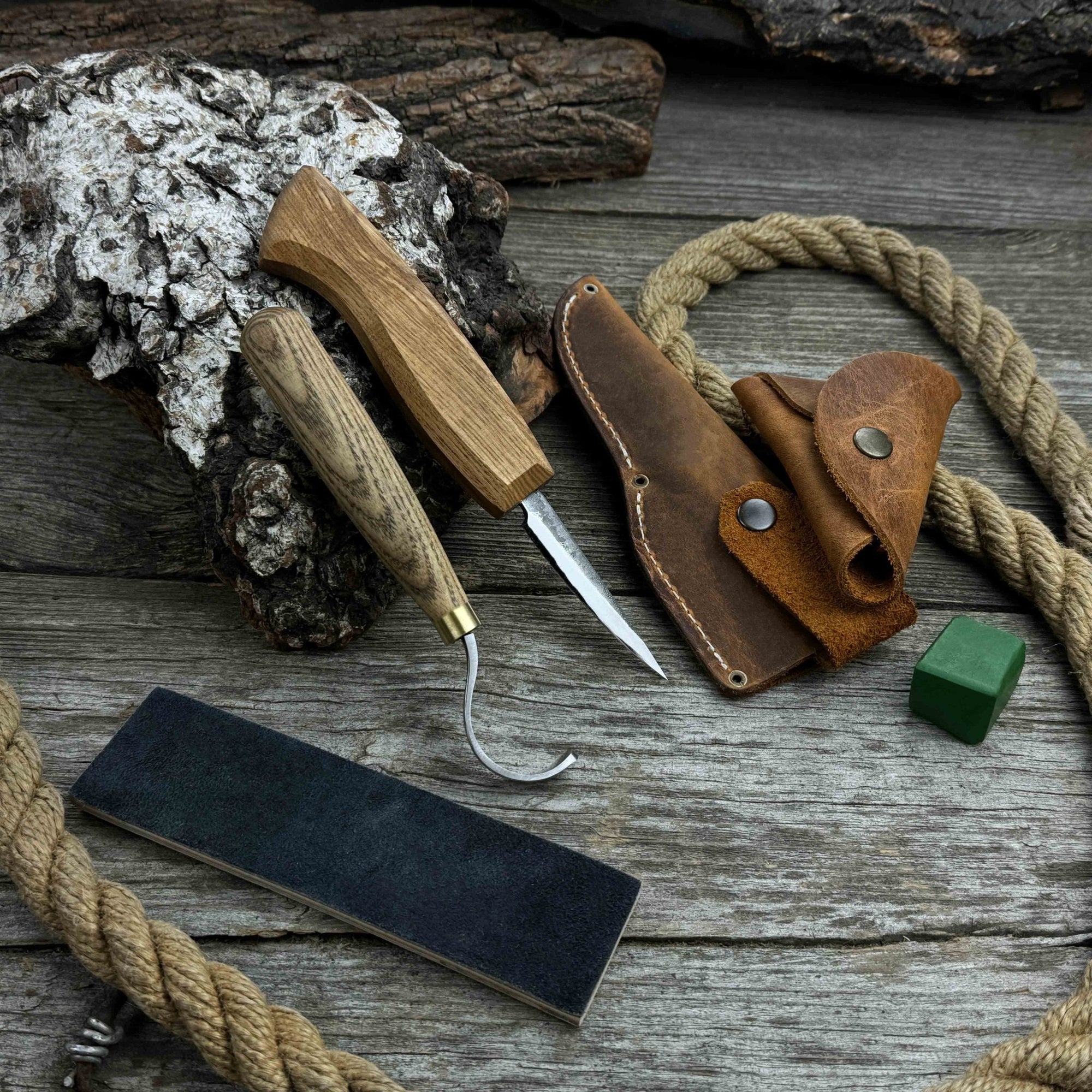 3-Piece Spoon Carving Tool Set with Leather Strop by Sharky Forged Steel Tools showing hook knife, sloyd knife, and leather strop on wooden surface