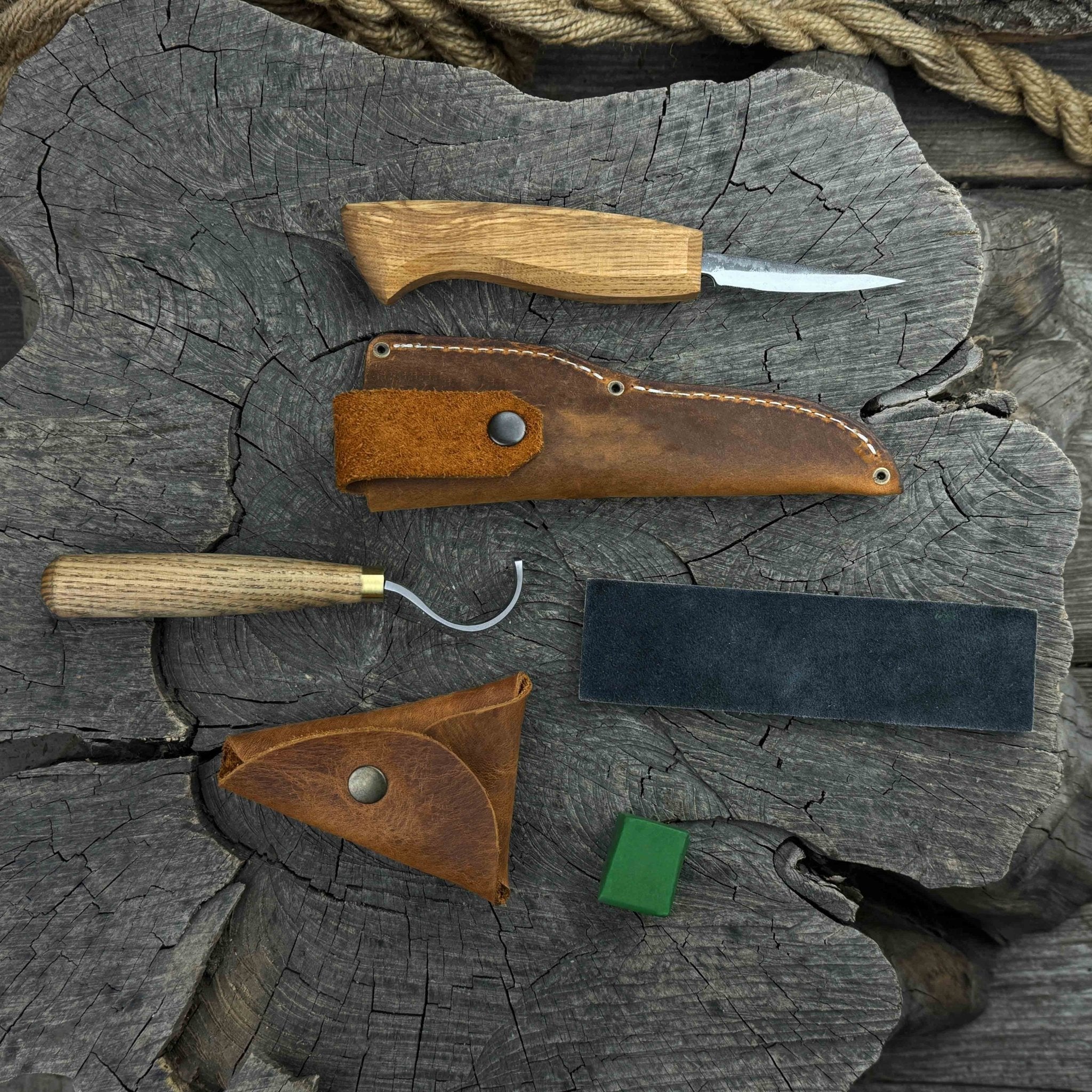 3-Piece Spoon Carving Tool Set with Leather Strop by Sharky Forged Steel Tools showing hook knife, sloyd knife, and leather strop on wooden surface