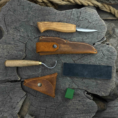 3-Piece Spoon Carving Tool Set with Leather Strop by Sharky Forged Steel Tools showing hook knife, sloyd knife, and leather strop on wooden surface