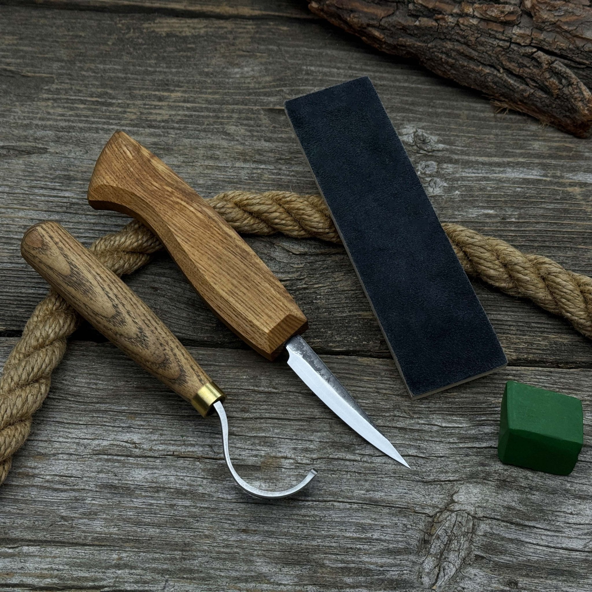3-Piece Spoon Carving Tool Set with Leather Strop by Sharky Forged Steel Tools showing hook knife, sloyd knife, and leather strop on wooden surface
