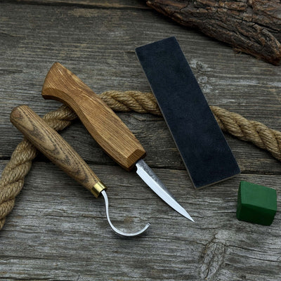 3-Piece Spoon Carving Tool Set with Leather Strop by Sharky Forged Steel Tools showing hook knife, sloyd knife, and leather strop on wooden surface