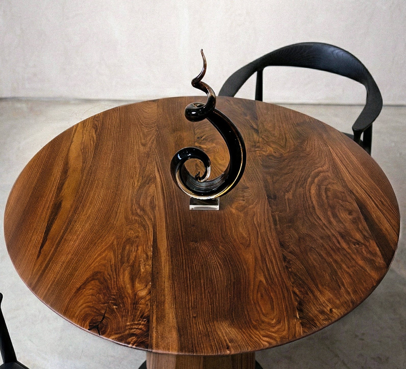 Modern round walnut dining table with sculptural pedestal base in a minimalist room