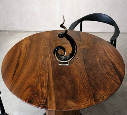 Modern round walnut dining table with sculptural pedestal base in a minimalist room