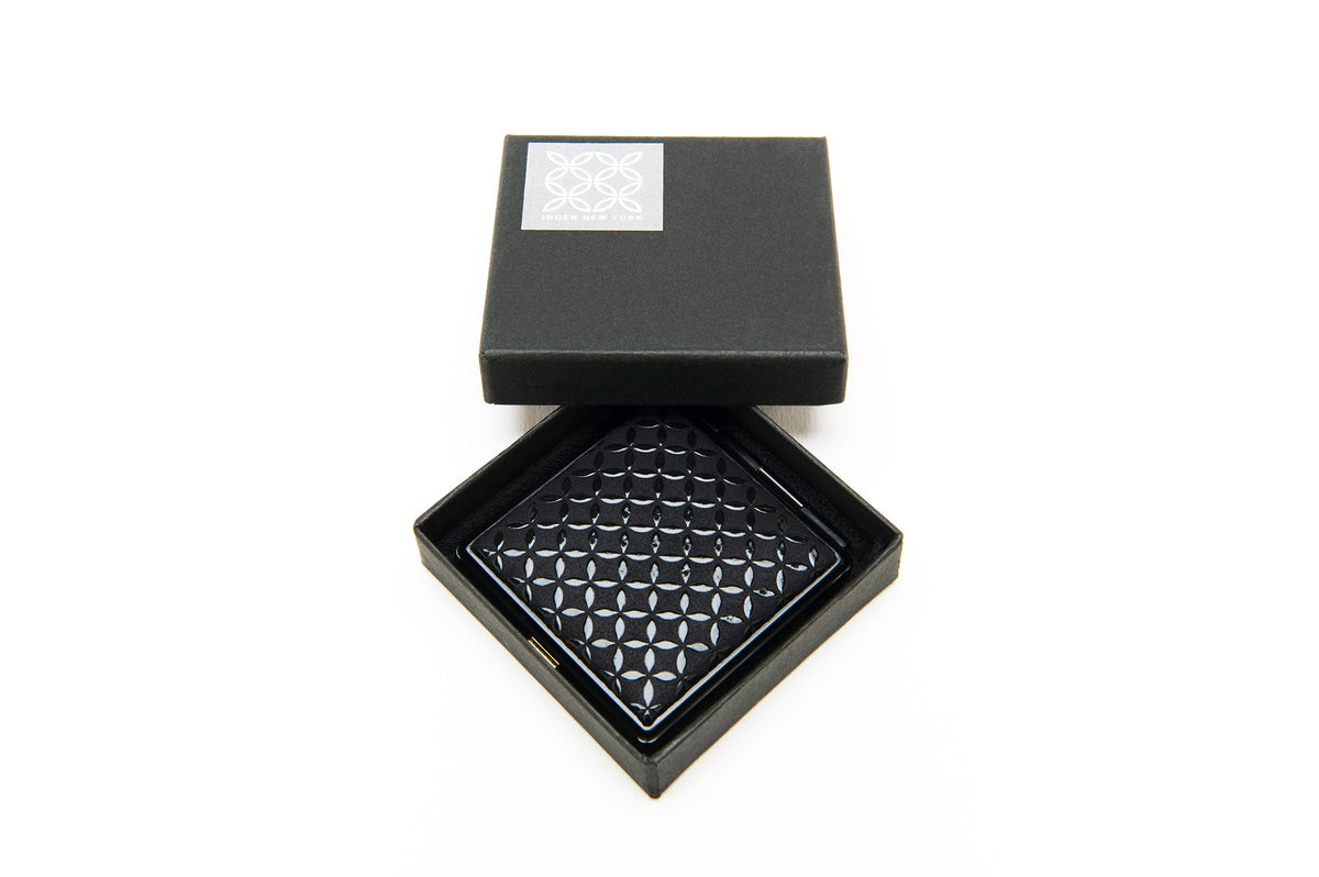 Black lacquered square tray with a raised interlocking circle pattern, presented inside a black box with a white decorative logo on the lid.