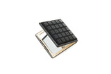 Compact square hand mirror with a black cover featuring a grid of raised pyramid studs, slightly open showing a silver reflective interior frame.