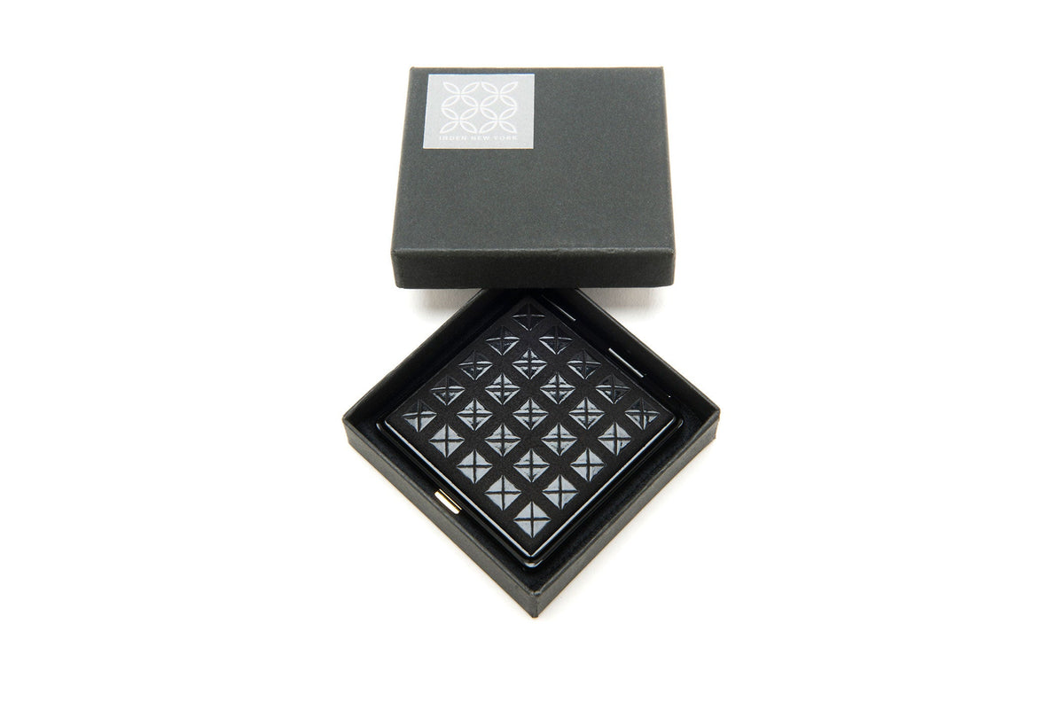 Black leather wallet with triangular stud pattern, displayed open inside a black square box with a silver decorative emblem on the lid.