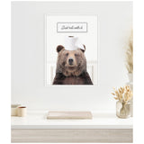 Framed canvas on a white wall featuring a brown bear wearing a roll of toilet paper like a headband, with text above saying 'Just roll with it.'