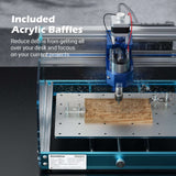 Desktop CNC router actively milling a rectangular wooden block with clear acrylic baffles around the spindle to contain debris on a perforated metal work surface.