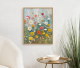 Framed floral print featuring colorful wildflowers in shades of yellow, pink, white, and orange against a soft blue and green background, hung on a white wall above a brass round table.