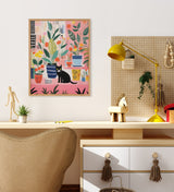 Whimsical painting of various potted houseplants on a pink background with a black cat sitting among them, framed and hung above a modern wooden desk.