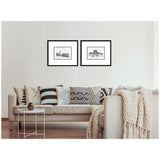Two black-framed vintage postcard prints of London and Paris landmarks hanging above a beige sofa adorned with patterned black-and-white cushions and a cream knitted throw.