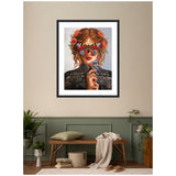 Framed wall art of a woman with red hair decorated with flowers, wearing a butterfly mask and holding a bluebird, against a beige and green room background with wooden bench and plants.
