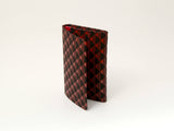 Red and black checkered Takane business card case standing open on a white background, showing its textured exterior pattern.