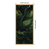 Aerial view of a winding white river flowing through a lush green valley with steep moss-covered cliffs, displayed in a vertical wooden frame.