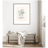 Line drawing of wildflowers in a curvy vase with a pale pink background, framed and hung above a wooden bench with a book and draped fabric in a neutral room.