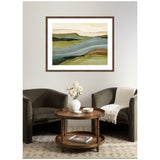Abstract landscape wall art featuring layered green, blue, brown, and beige hues, framed in dark wood, hanging above a sitting area with two dark armchairs and a round wooden table.