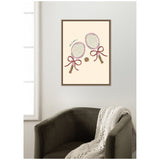 Framed canvas featuring stylized tennis rackets with pink bows and a tennis ball, hanging above a dark olive armchair with a white knitted throw draped over one arm.