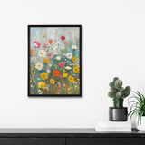 Framed canvas print of a wildflower garden featuring red, yellow, white, and pink flowers with green stems and a soft blue-gray background, hanging above a dark wood surface with potted cactus and desk plant.