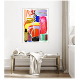 Abstract framed canvas with colorful shapes in red, orange, blue, pink, black, and green hung above a wooden bench with a white cloth and open book in a bright room.