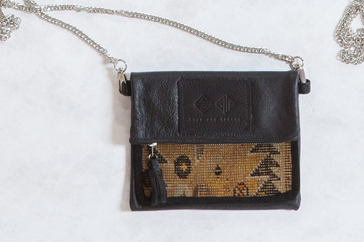 Antique Caucasian Rug Fragment Bag showing blue, red, and cream rug fragment with folded brown leather top and metal chain strap.