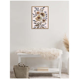 Framed canvas with muted floral design of beige and green flowers and dark blue leaves above white bench draped with cream fur throw, beige bag on floor.