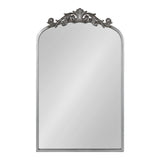 Rectangular mirror with an arched top, framed in silver metal, featuring intricate ornamental scrollwork and leaf motifs at the top center.