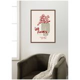 Abstract red floral line drawing with green striped vase and red cursive text reading 'les fleurs' on light background, framed and hung above dark green chair with beige knit throw.